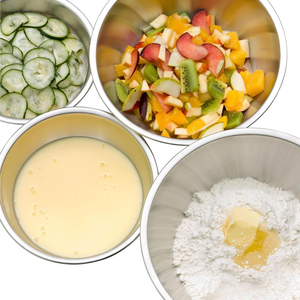 Quatre bols en acier inoxydable : rondelles de concombre, salade de fruits, liquide crémeux, farine avec beurre.