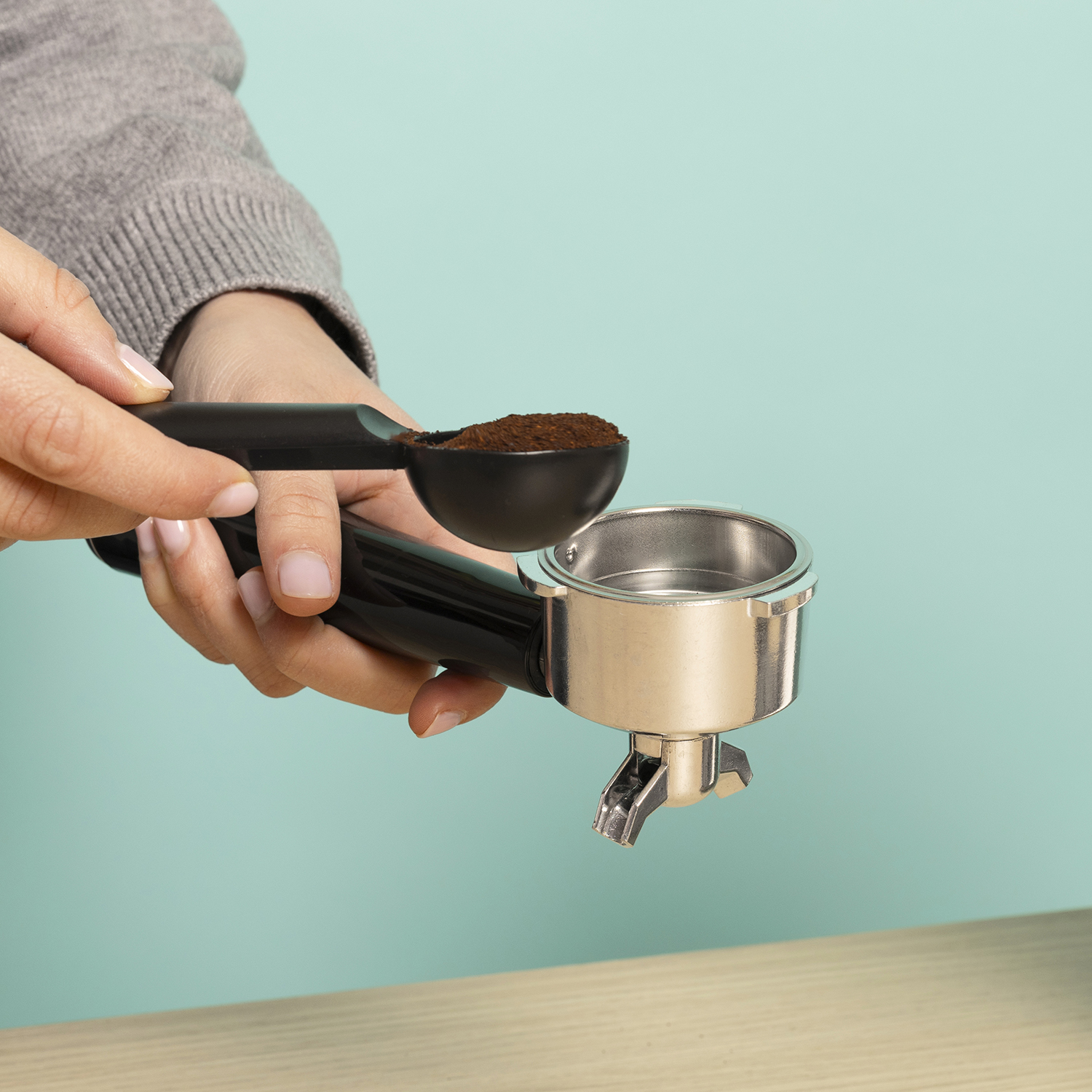 Una mano sostiene una cuchara de café molido sobre un portafiltro de espresso.