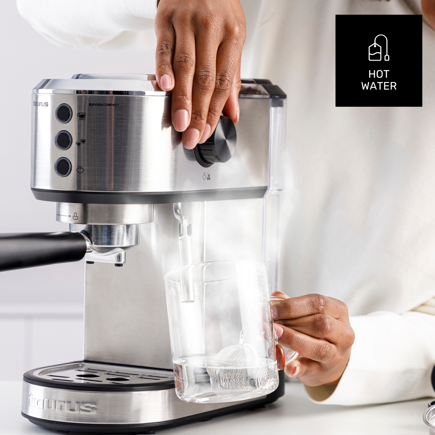 Una mano sostiene un vaso mientras sale agua caliente de una máquina de espresso.