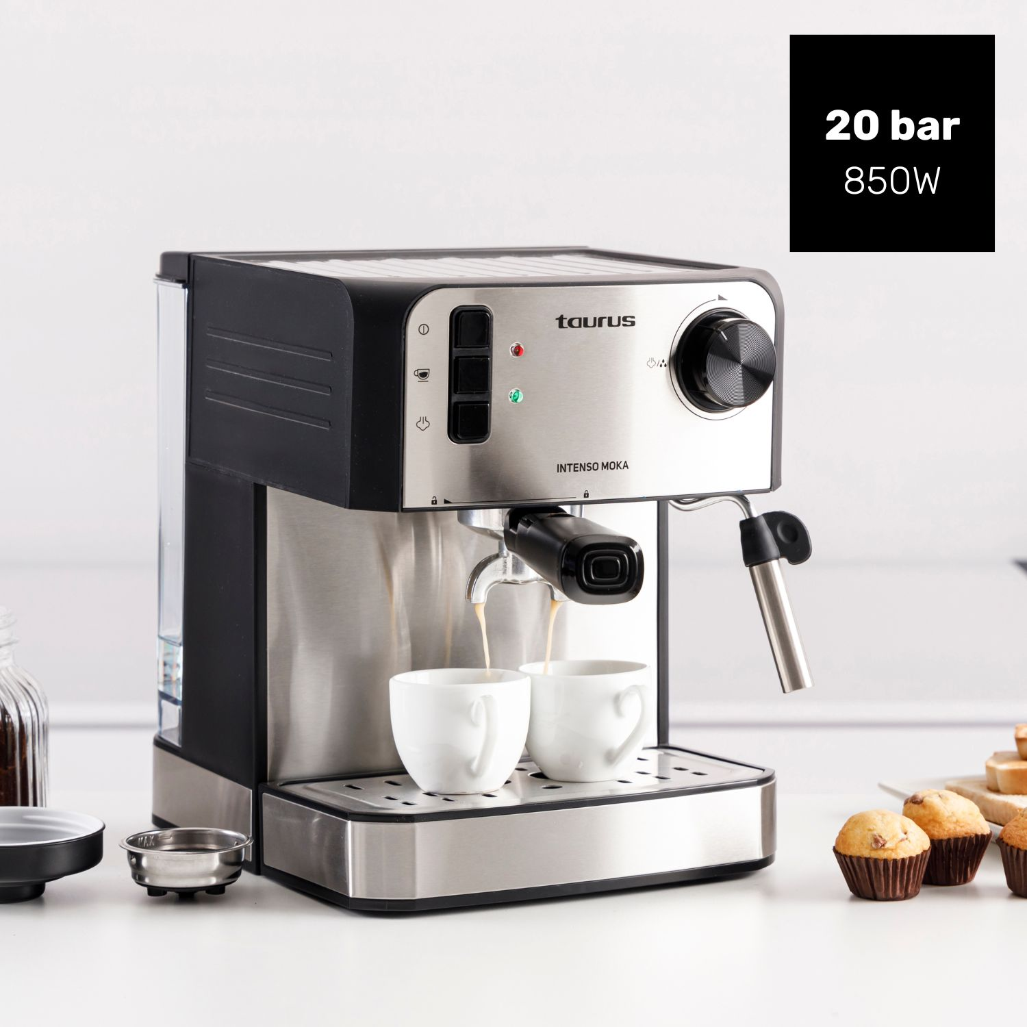 Una cafetera Taurus prepara café en dos tazas blancas. Hay magdalenas cerca.