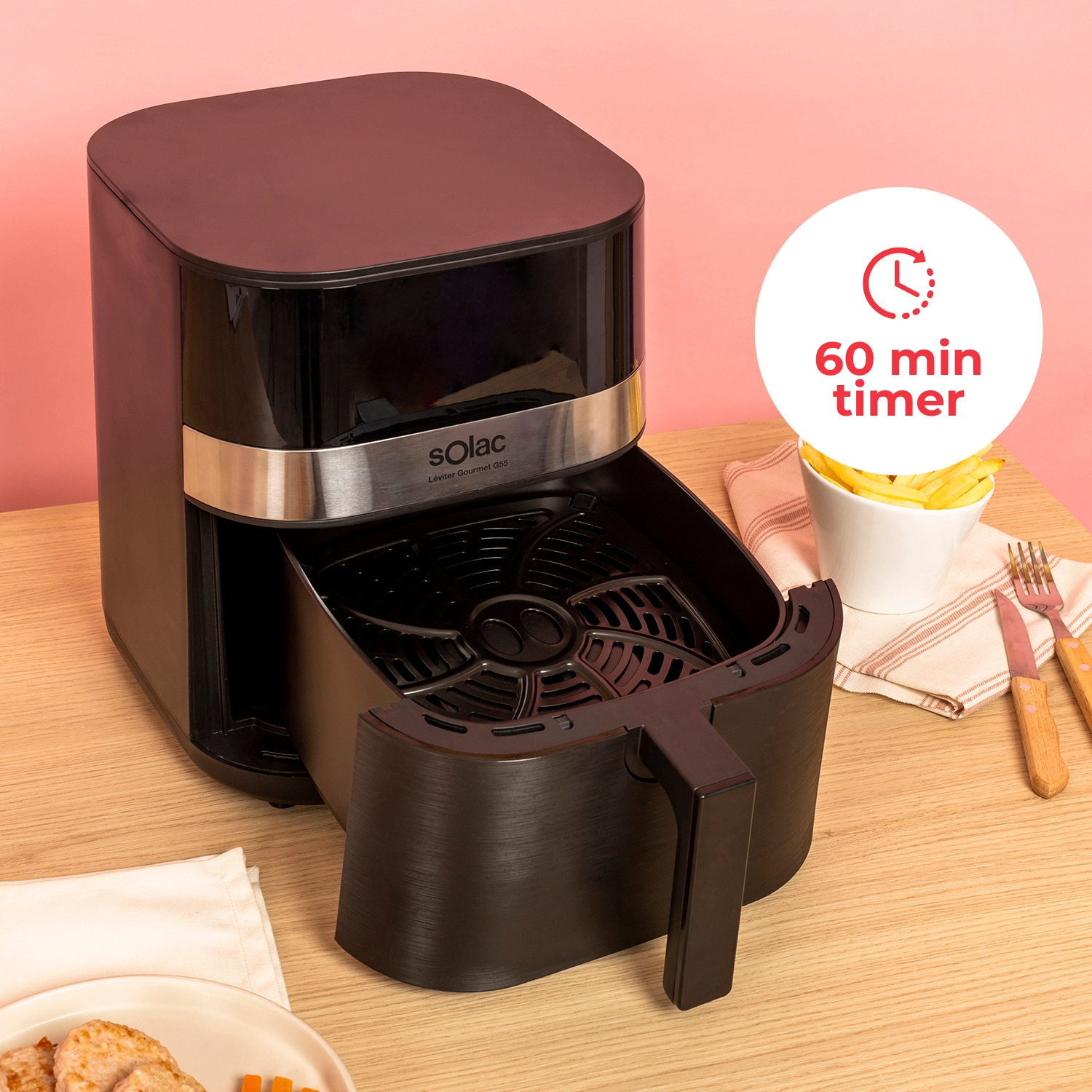 Freidora de aire negra con cesta abierta, patatas fritas y cubiertos al lado.
