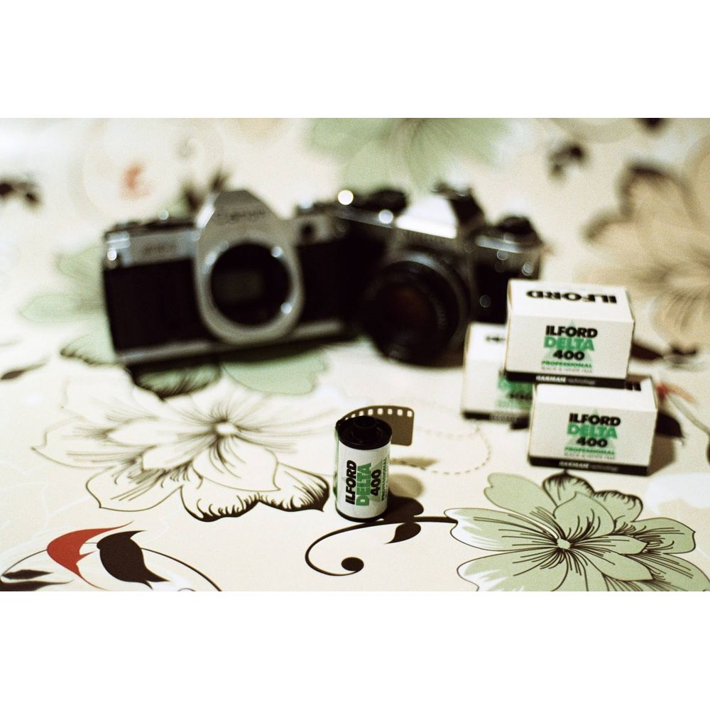 Stary aparat fotograficzny i rolki filmu na wzorzystym obrusie.