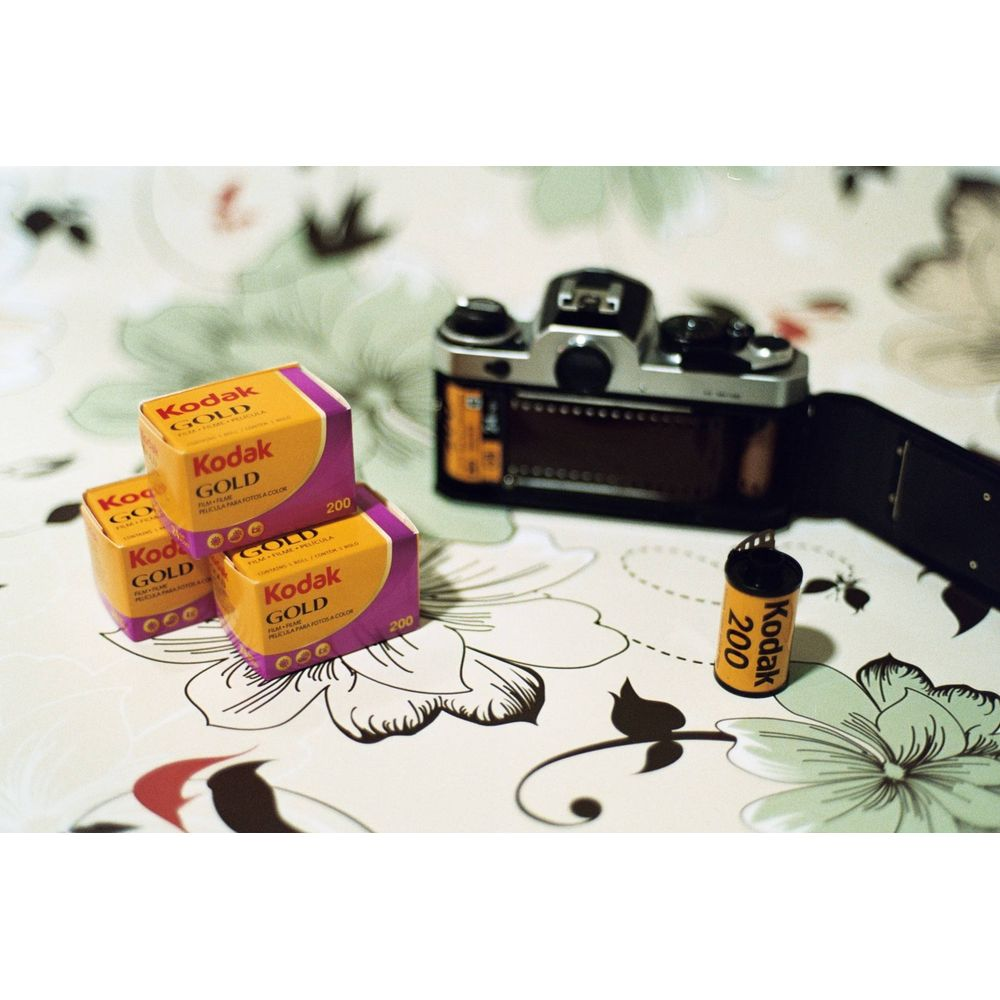 Trois boîtes de film Kodak Gold et une pellicule à côté d'un appareil photo.