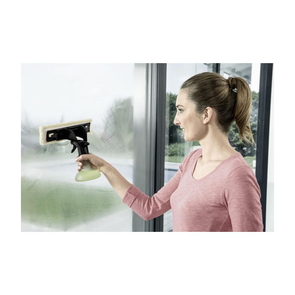 Frau mit einem Fensterreiniger, der eine Scheibe besprüht.