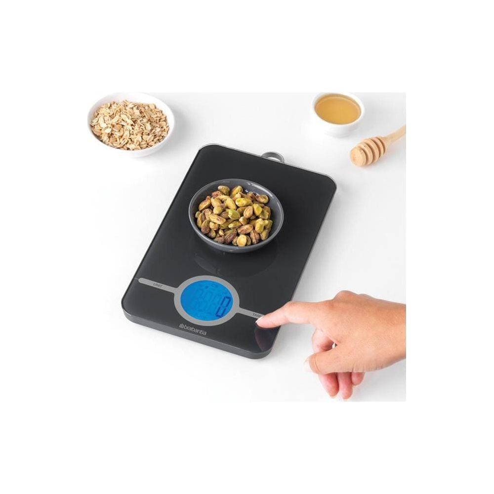 Eine digitale Küchenwaage mit Schüssel Pistazien, Haferflocken und Honig.