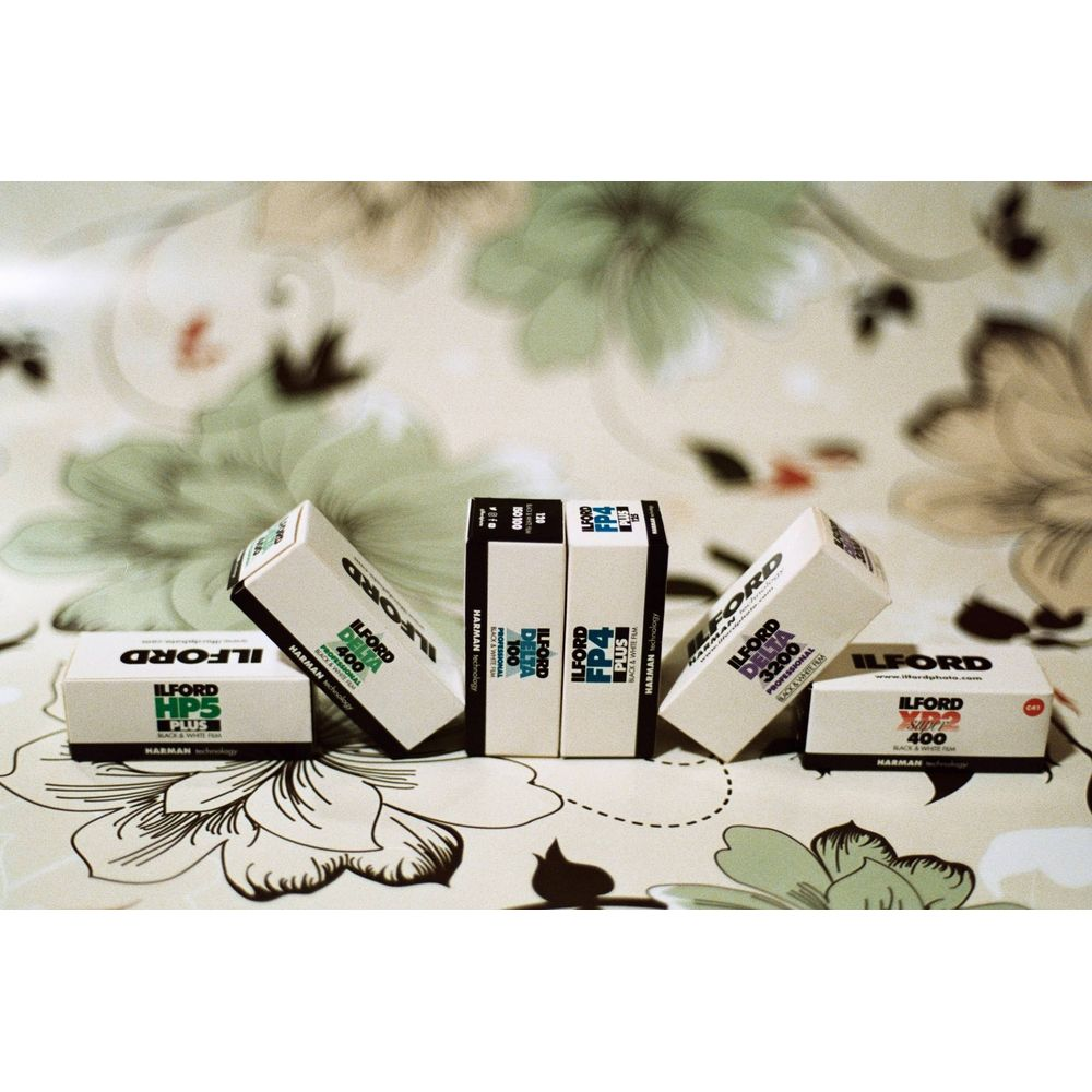 Cinco cajas de película Ilford de varios tipos dispuestas sobre un paño floral.
