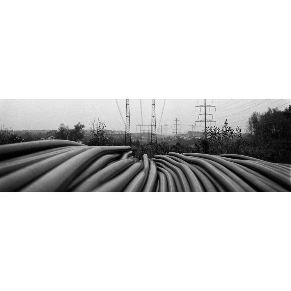 Duże zwoje kabli na pierwszym planie, słupy energetyczne i drzewa w tle.