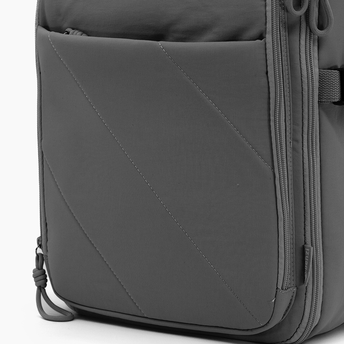 Mochila gris con costuras diagonales y cremalleras.