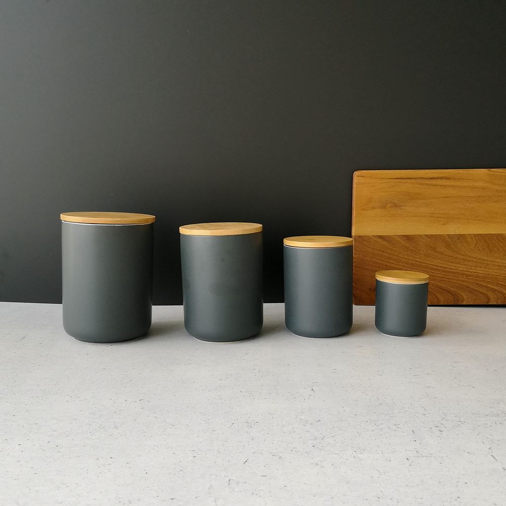 Vier graue Vorratsdosen unterschiedlicher Größe mit Holzdeckeln auf einem Tisch.