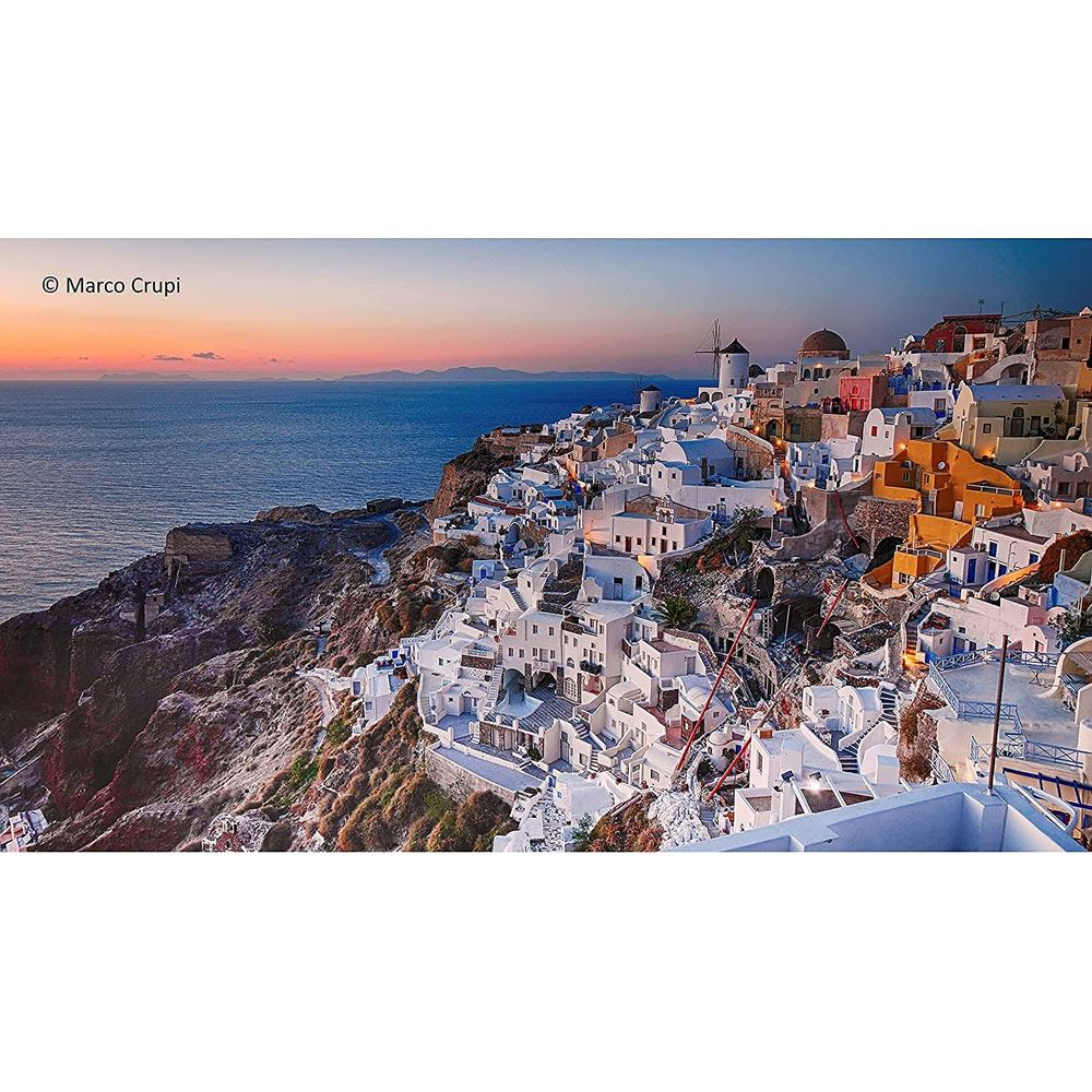 Białe budynki na klifie nad morzem o zachodzie słońca, z wiatrakiem.