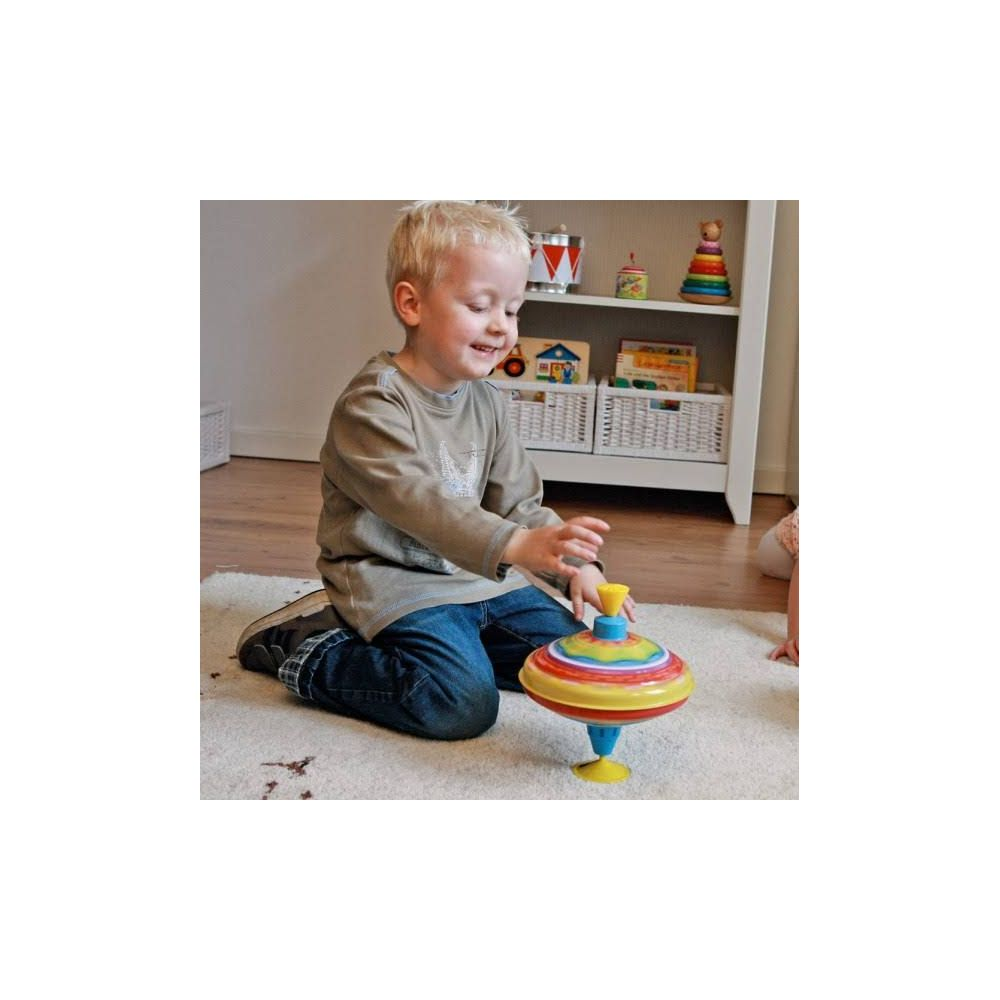 Chłopiec bawi się kolorową bączkiem na dywanie.