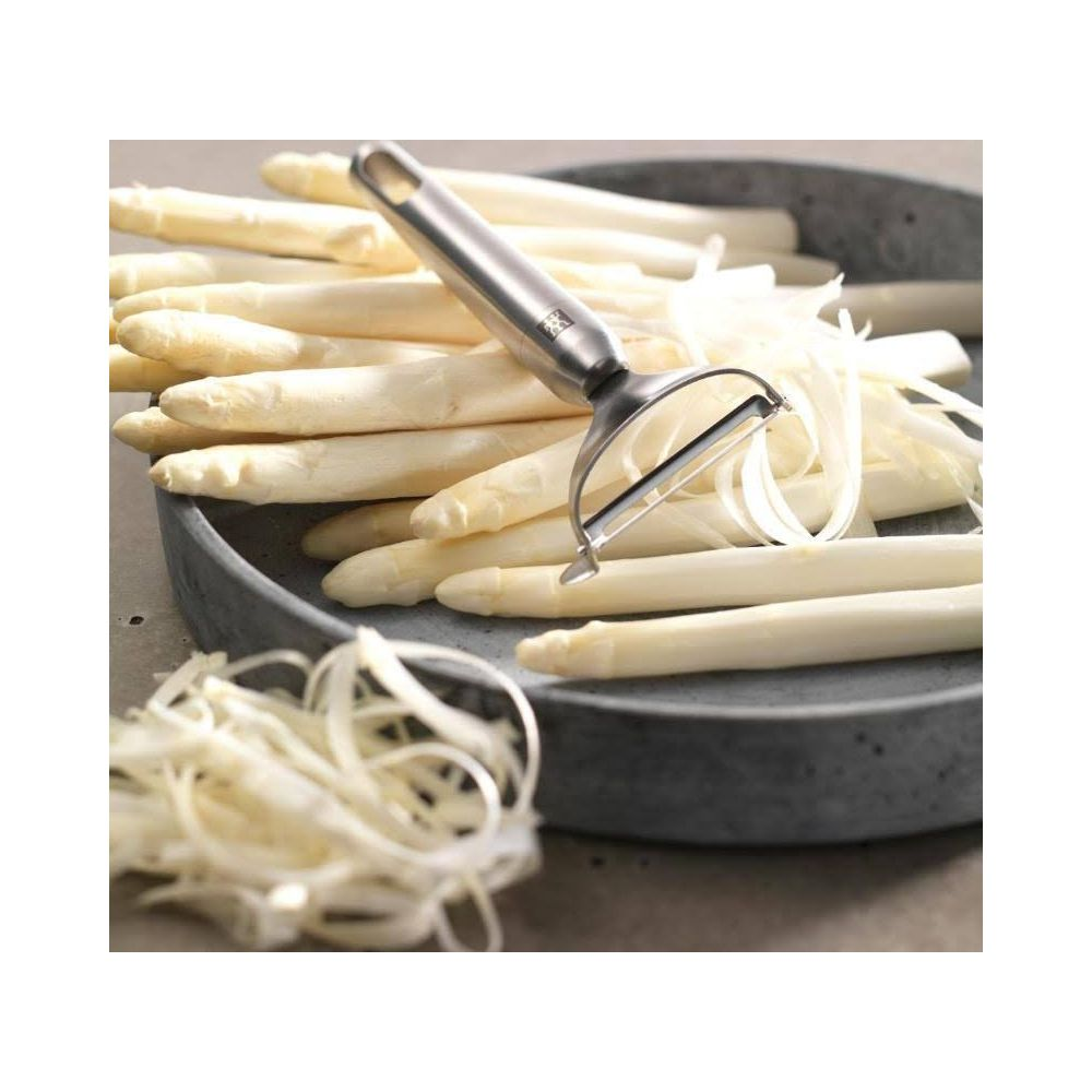 Obieraczka leży na stosie białych szparagów w misce.