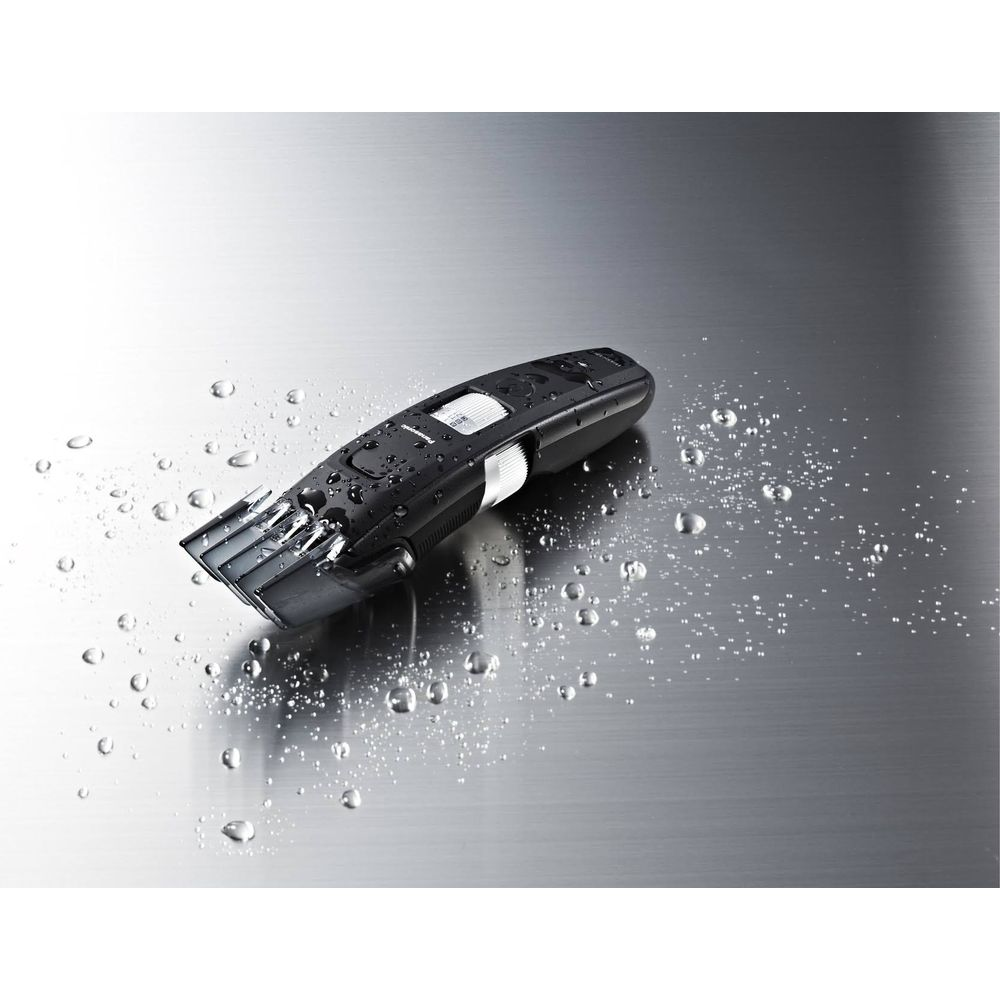 Ein schwarzer Haarschneider liegt auf einer metallischen Oberfläche mit Wassertropfen.