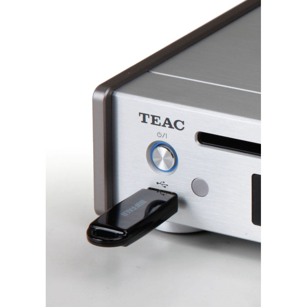 Una memoria USB negra está conectada a un dispositivo TEAC plateado con un botón azul.