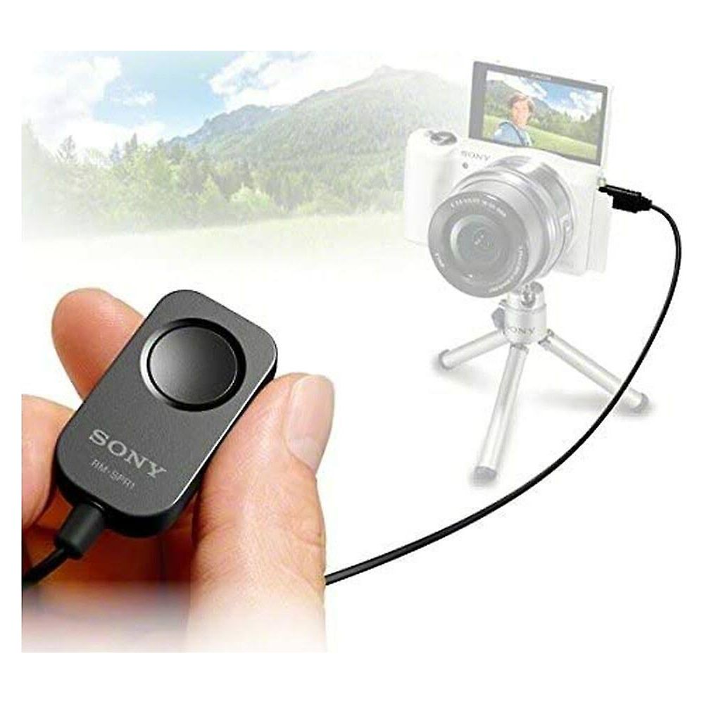Eine Hand hält eine Sony Fernbedienung, daneben steht eine Kamera auf einem Stativ.