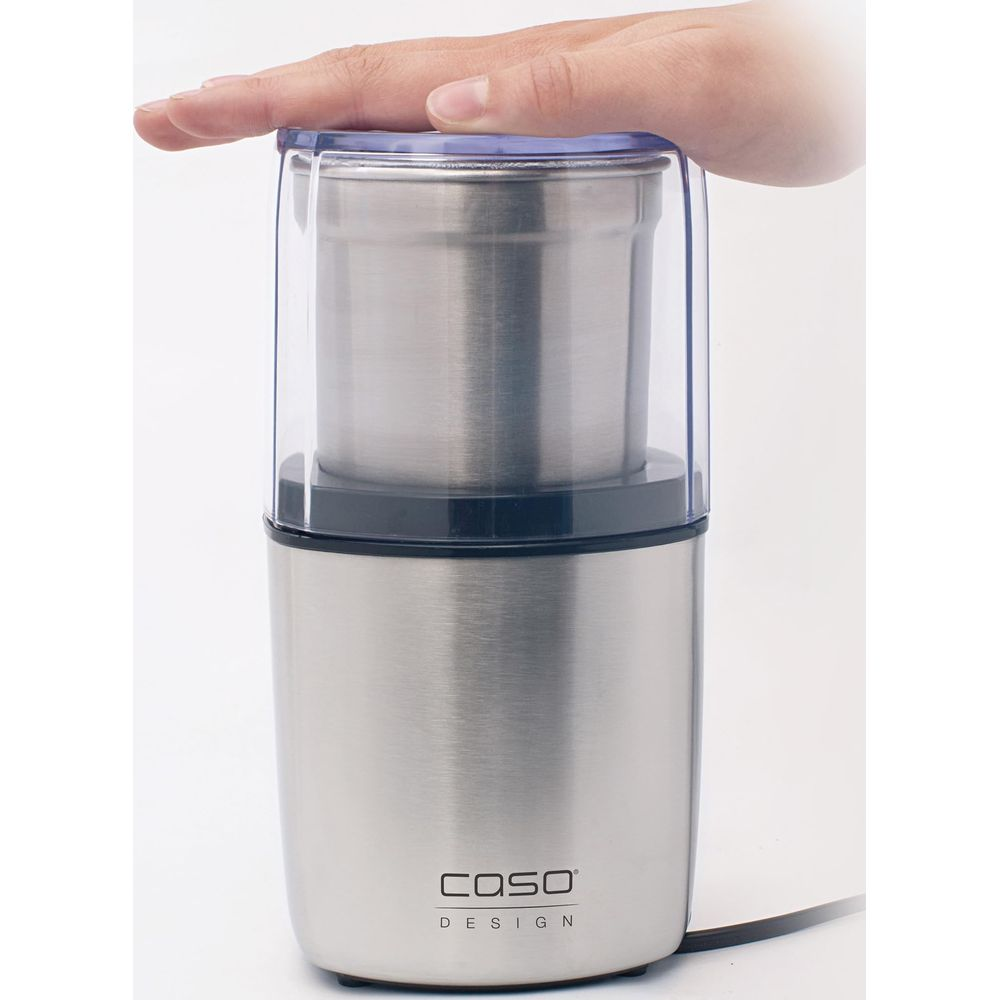 Moulin à café argenté en acier inoxydable avec couvercle transparent, tenu par une main.