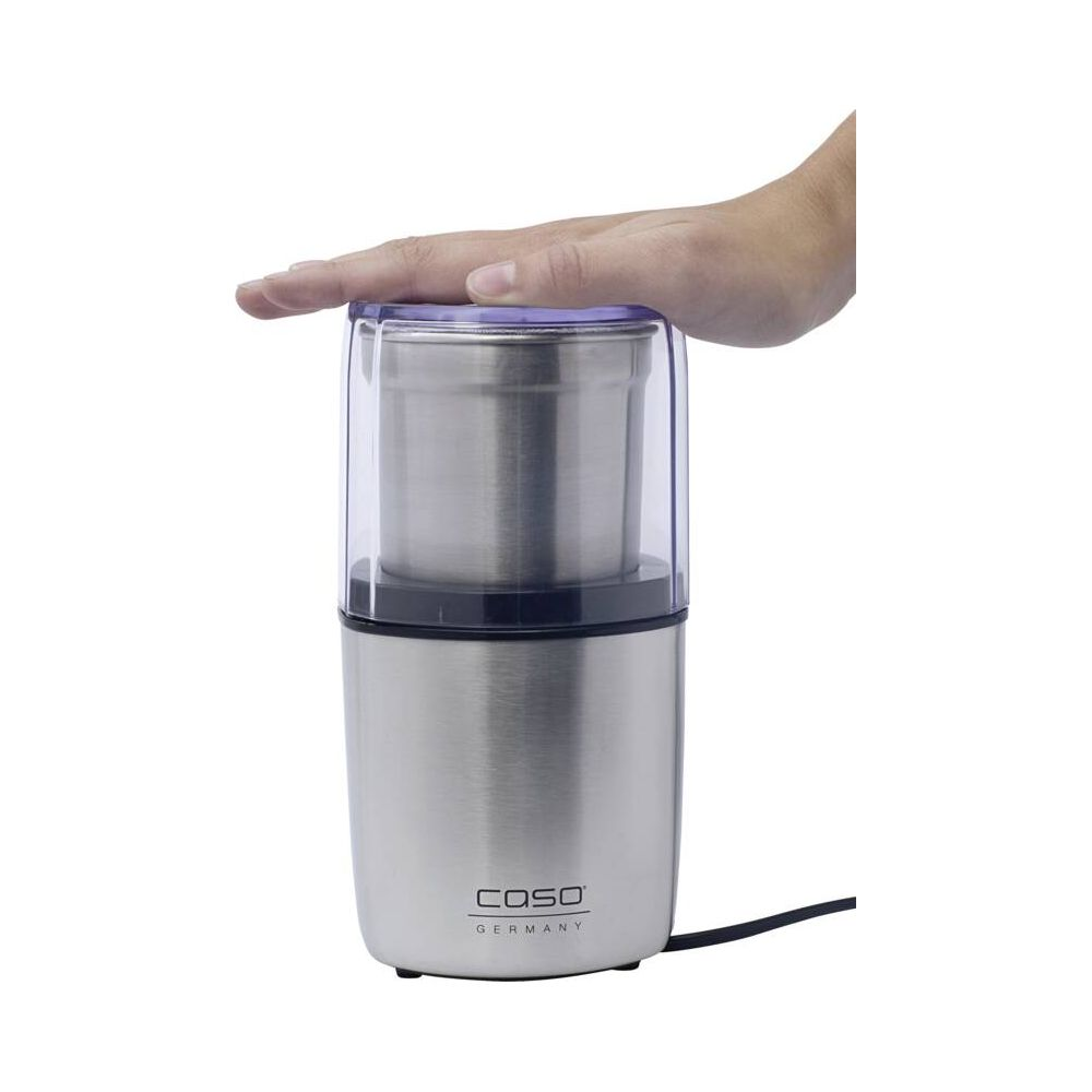 Une main appuie sur le couvercle transparent d'un moulin à café électrique argenté.