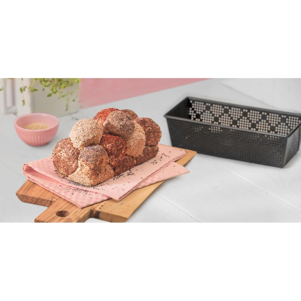 Ein Laib Brot mit mehreren Brötchen, bestreut mit Samen, auf einem Holzbrett mit einer Schüssel daneben.