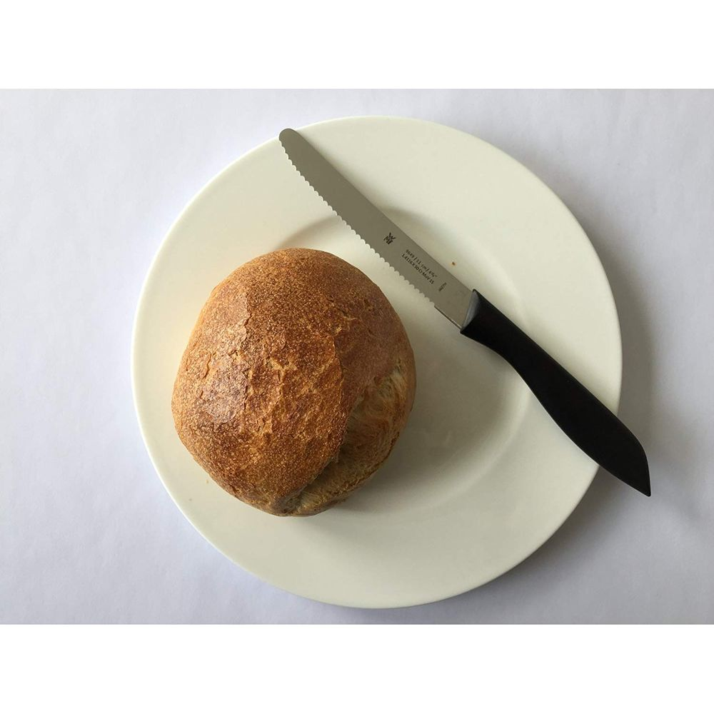 Un seul petit pain sur une assiette blanche avec un couteau à pain à côté.