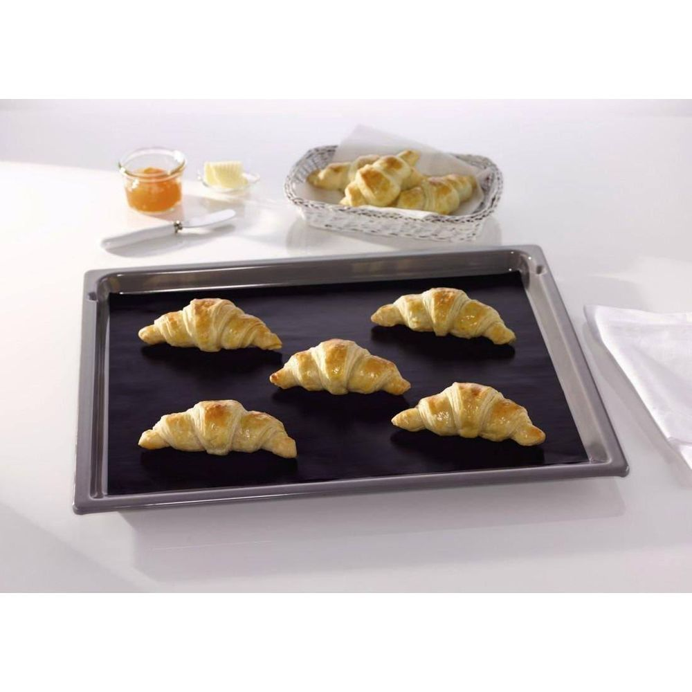 Fünf goldbraune Croissants liegen auf einem Backblech mit schwarzer Matte. Daneben sind ein Glas Marmelade und Butter.