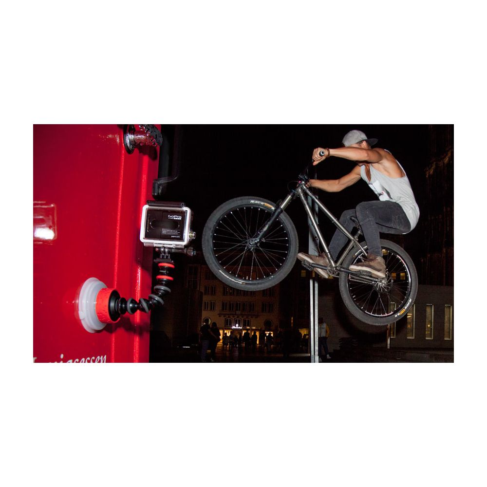 Ciclista BMX salta di notte, telecamera GoPro filma su superficie rossa.