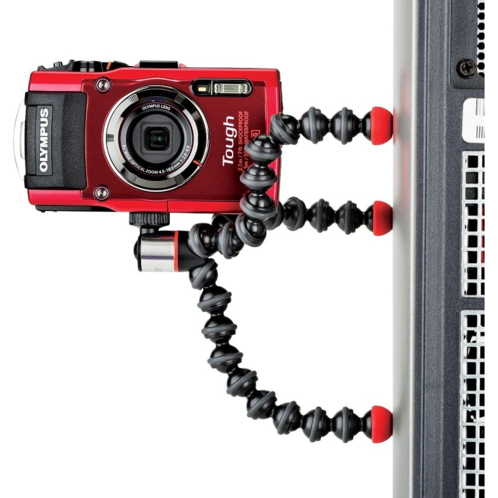Eine rote Olympus Tough Kamera ist an einem flexiblen Gorillapod-Stativ befestigt, das an einer grauen Oberfläche haftet.