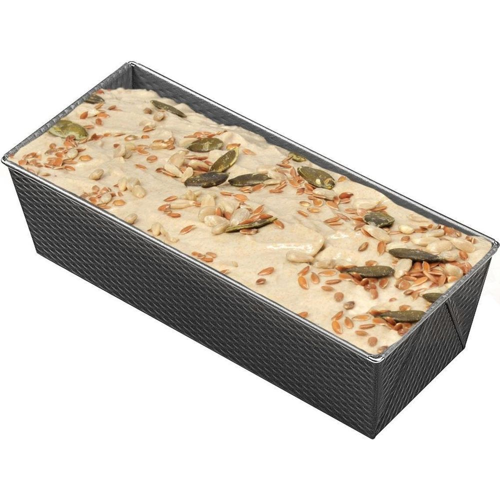 Ein Brotlaib aus Teig mit Kernen in einer rechteckigen Backform.