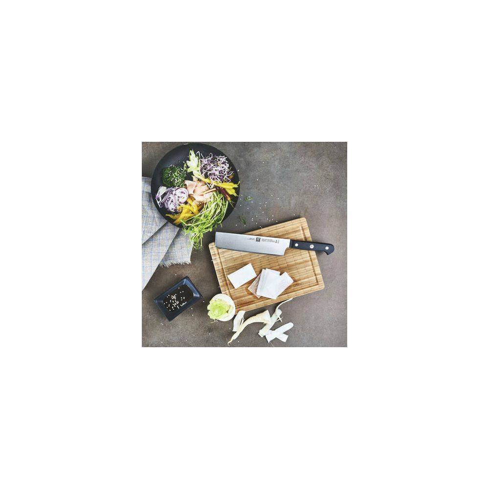 Nóż szefa kuchni leży na drewnianej desce obok miski warzyw i naczynia z sosem.