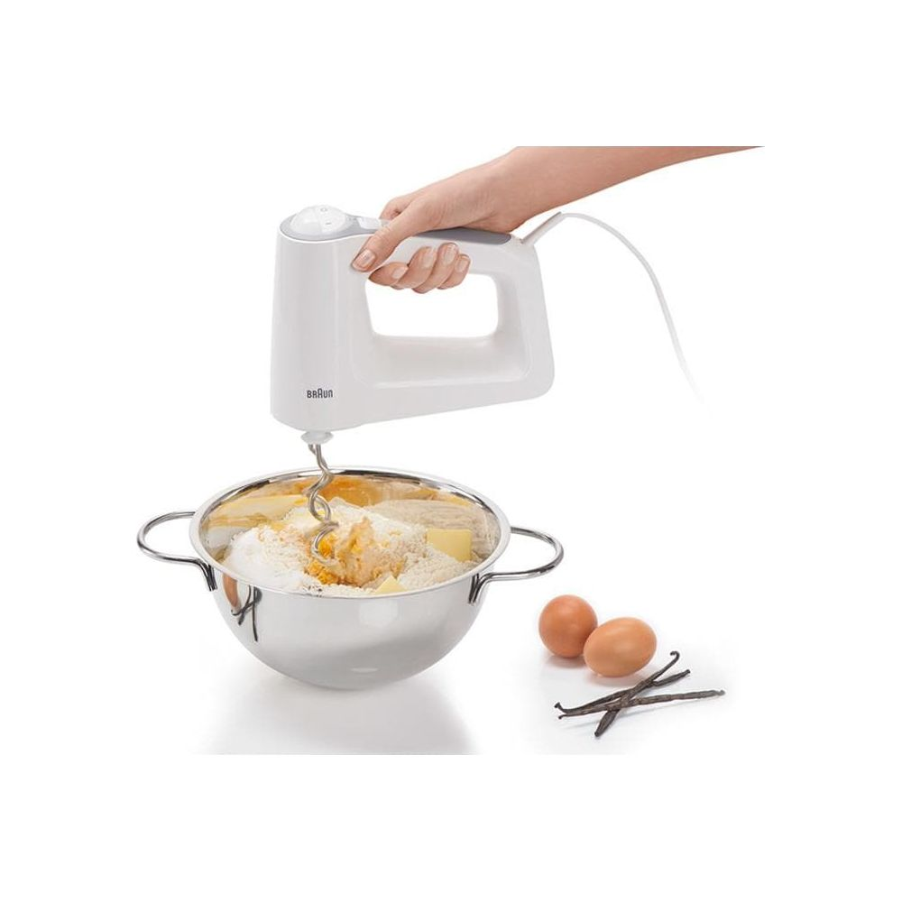Ręka używa białej mikser ręczny do mieszania składników w misce.