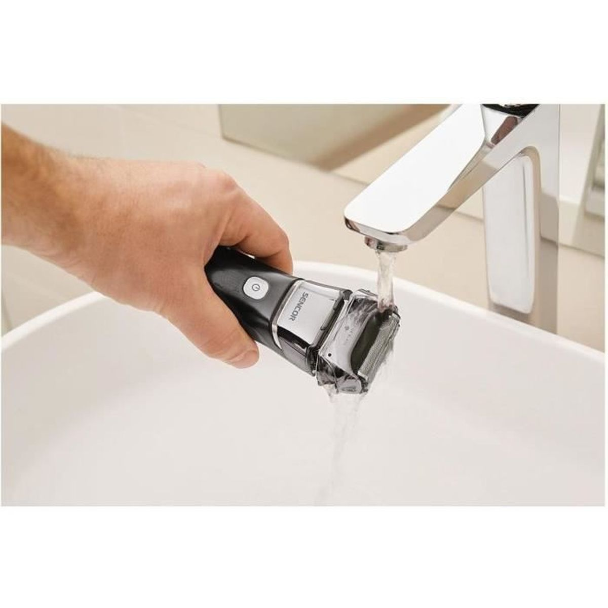 Un uomo sciacqua un rasoio elettrico nero sotto l'acqua corrente in un lavandino bianco.
