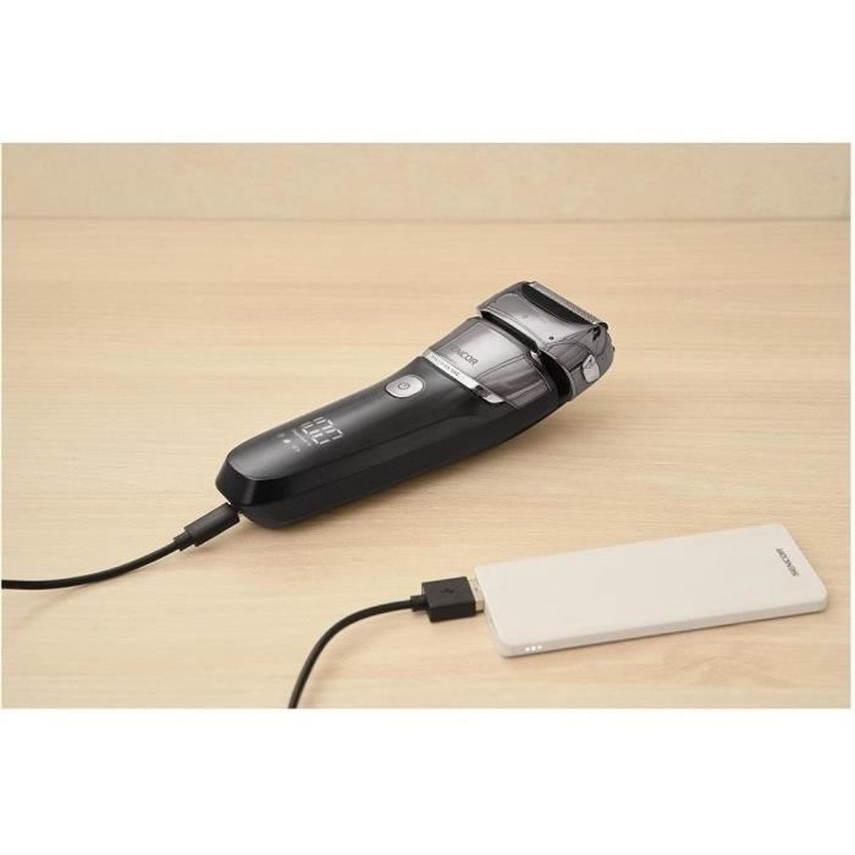 Un rasoio elettrico nero è collegato a un power bank bianco tramite cavo.