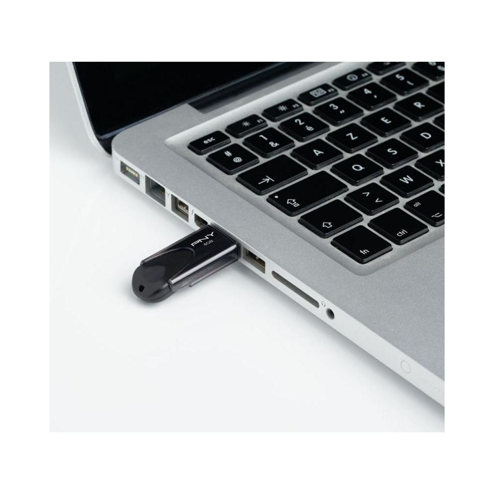 Czarny pendrive podłączony do srebrnego laptopa.