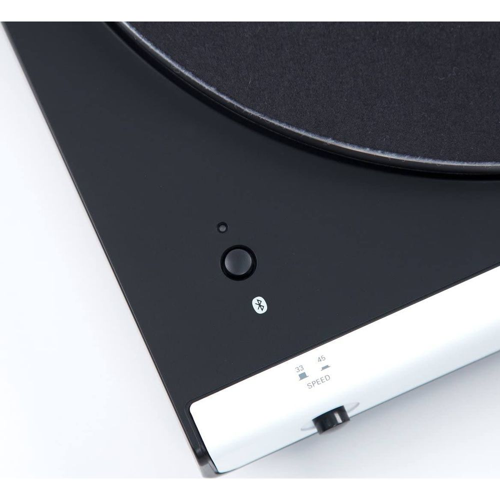 Nahaufnahme eines schwarzen Plattenspielers mit weißem Akzent, Geschwindigkeitsregler und Bluetooth-Symbol.