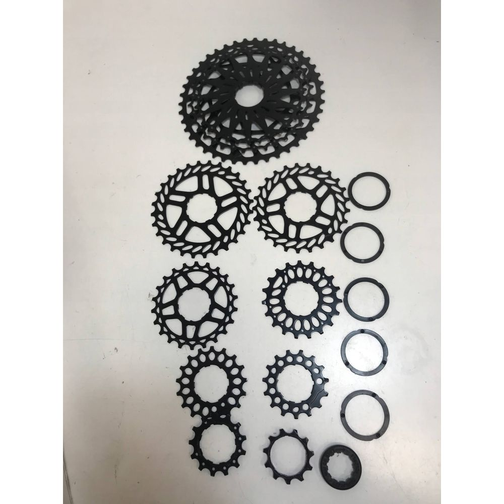 Czarne zębatki kasety rowerowej i pierścienie dystansowe na białej powierzchni.