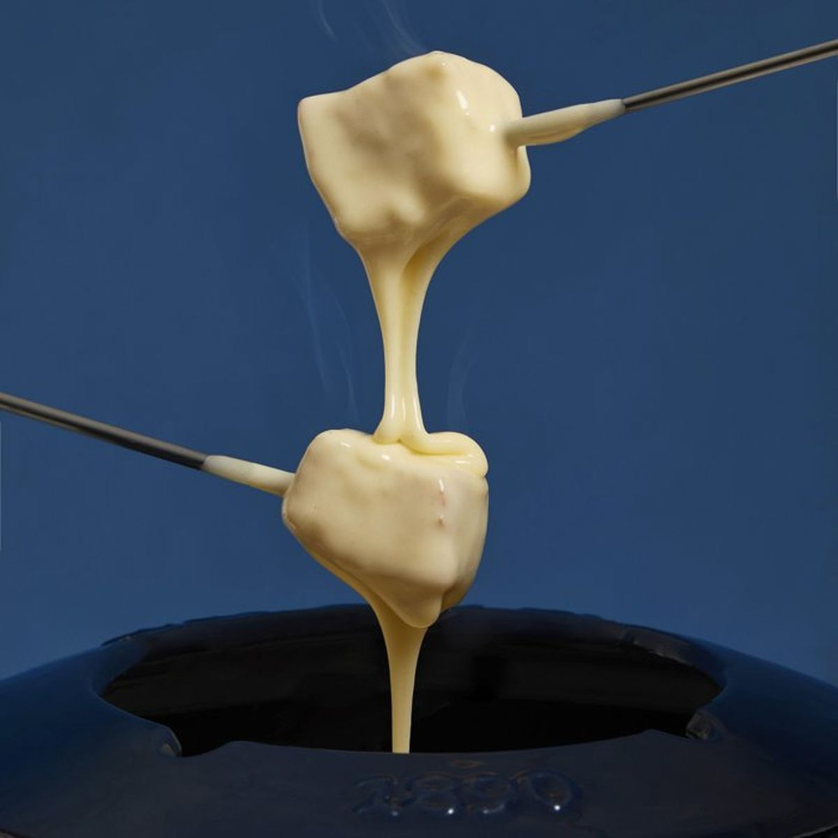 Käsefondue mit Brotstücken auf Gabeln, dampfend über einem dunklen Topf.
