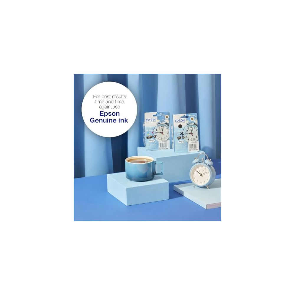 Una tazza di caffè blu siede su un piedistallo azzurro accanto a due confezioni di inchiostro Epson e una sveglia.