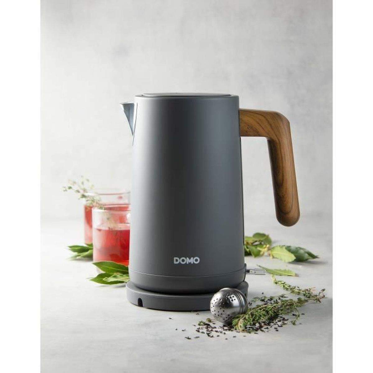 Grauer Wasserkocher mit Holzgriff, daneben Gläser mit rotem Getränk und Kräuter.