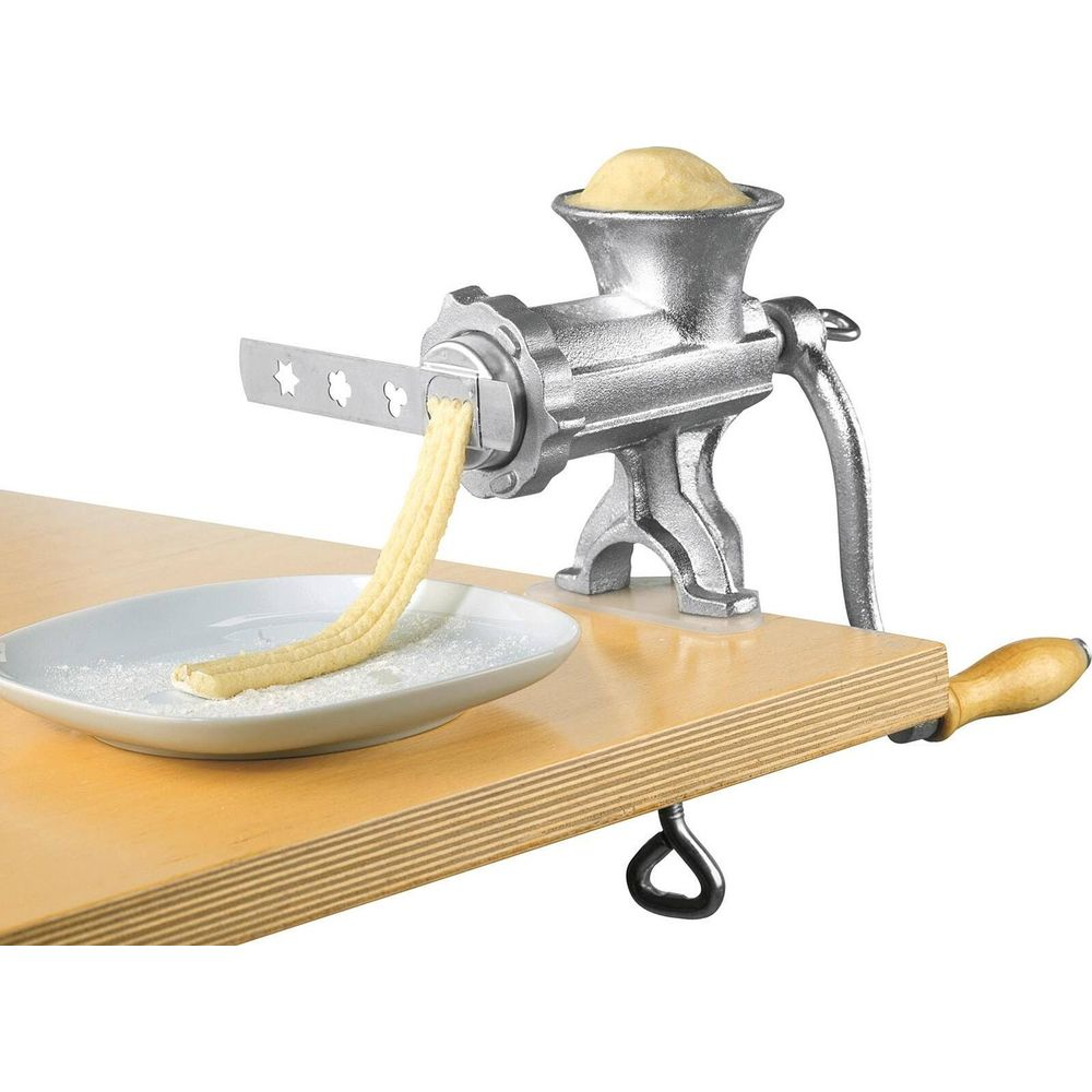 Una macchina per la pasta argentata estrude l'impasto attraverso una piastra a forma di stella su un piatto.