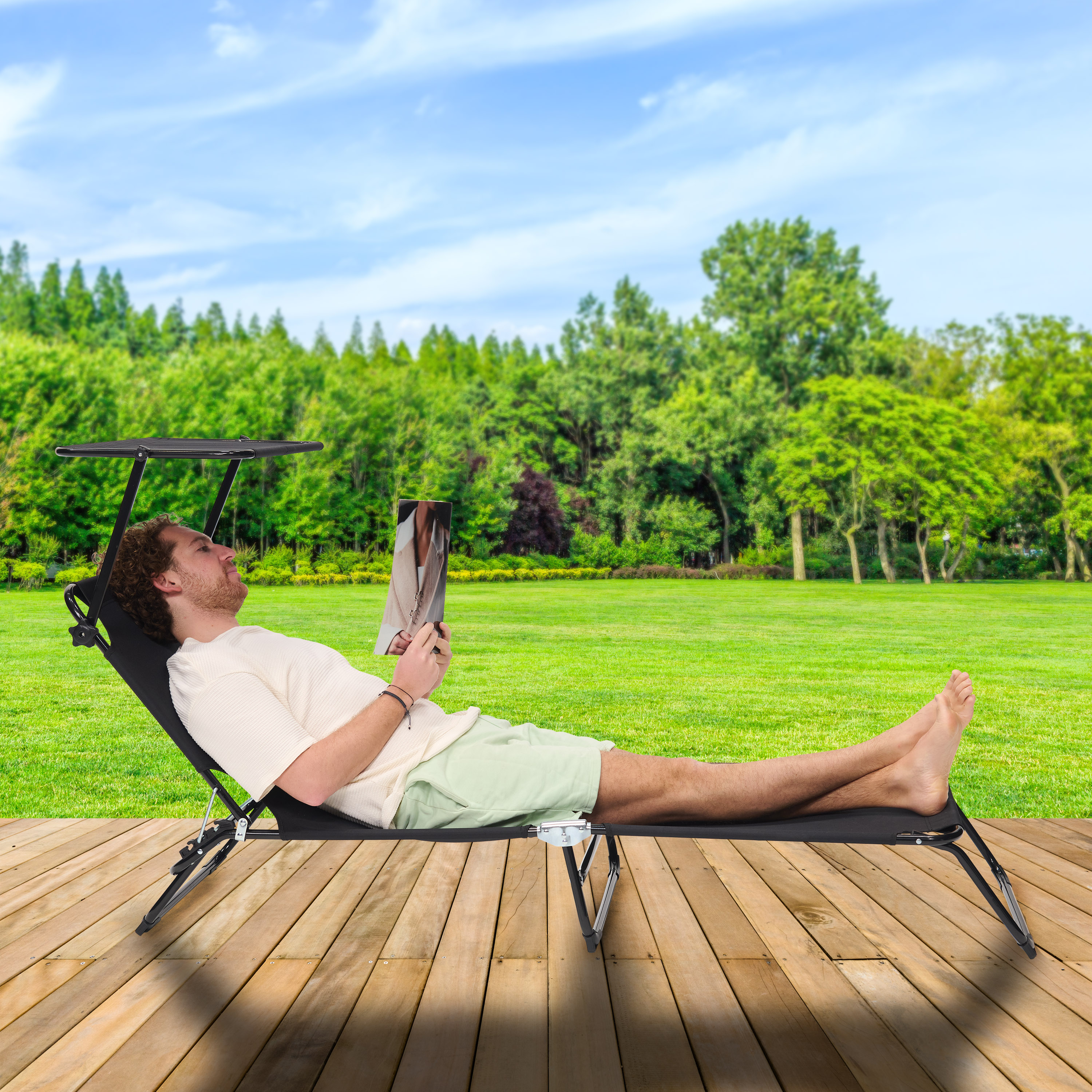 Man op ligstoel leest boek buiten op houten dek, groen gazon, bomen.