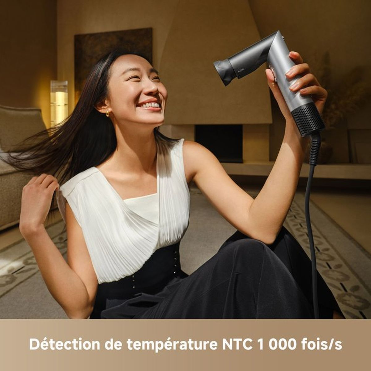 Kobieta z suszarką do włosów w pomieszczeniu. Uśmiecha się.