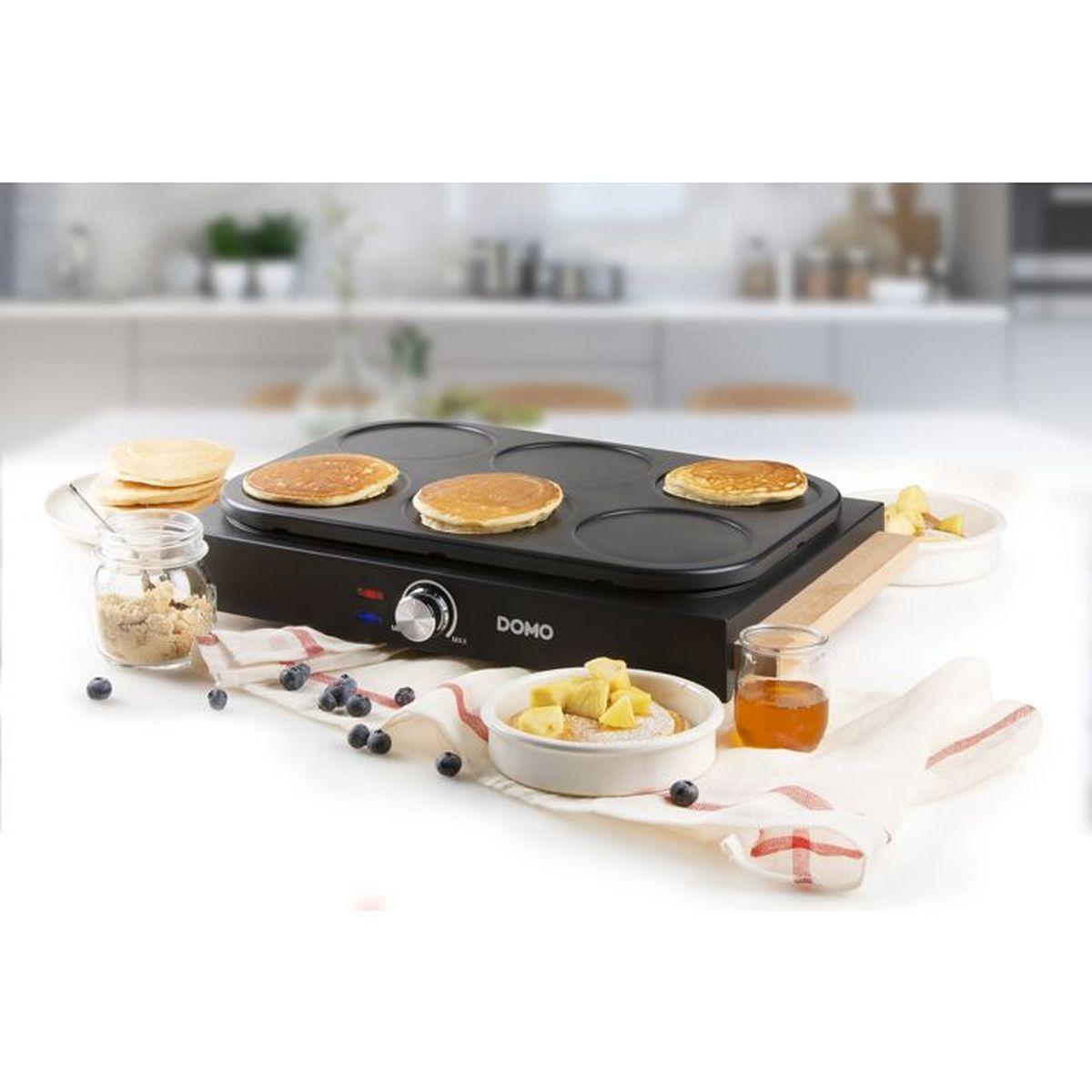 Ein Domo-Pfannkuchengrill mit Pfannkuchen, Beeren, Honig und Apfelstücken.