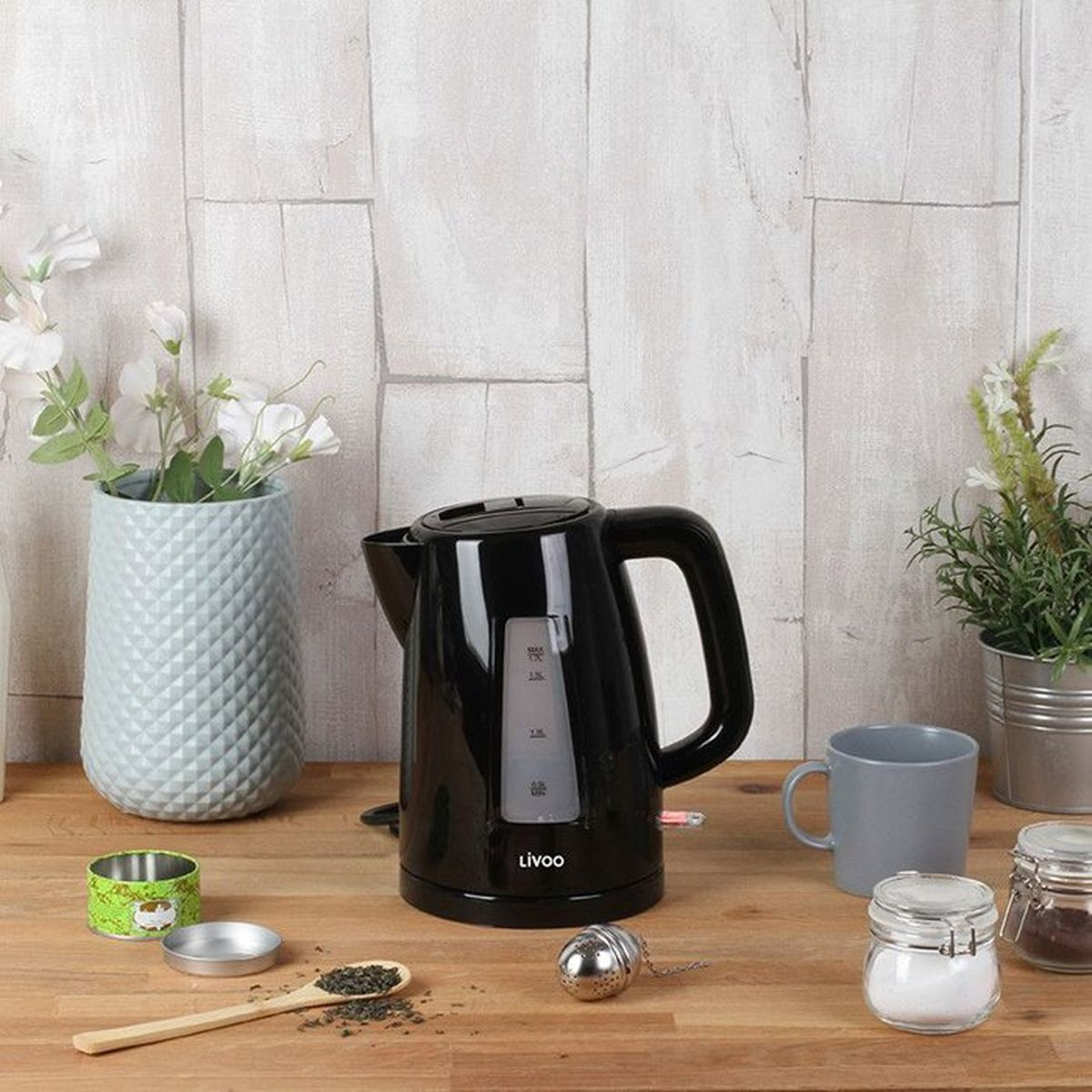 Czajnik elektryczny z łyżeczką, herbatą i kwiatami na drewnianym stole.