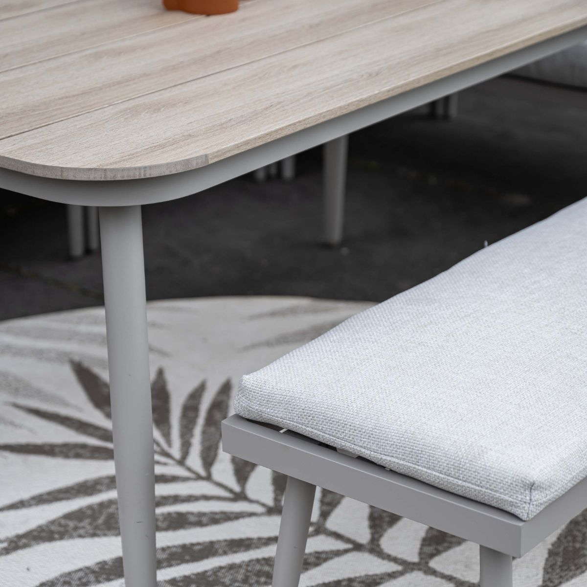 Houten tafel met grijze rand en grijs kussen op vloerkleed met bladmotief.