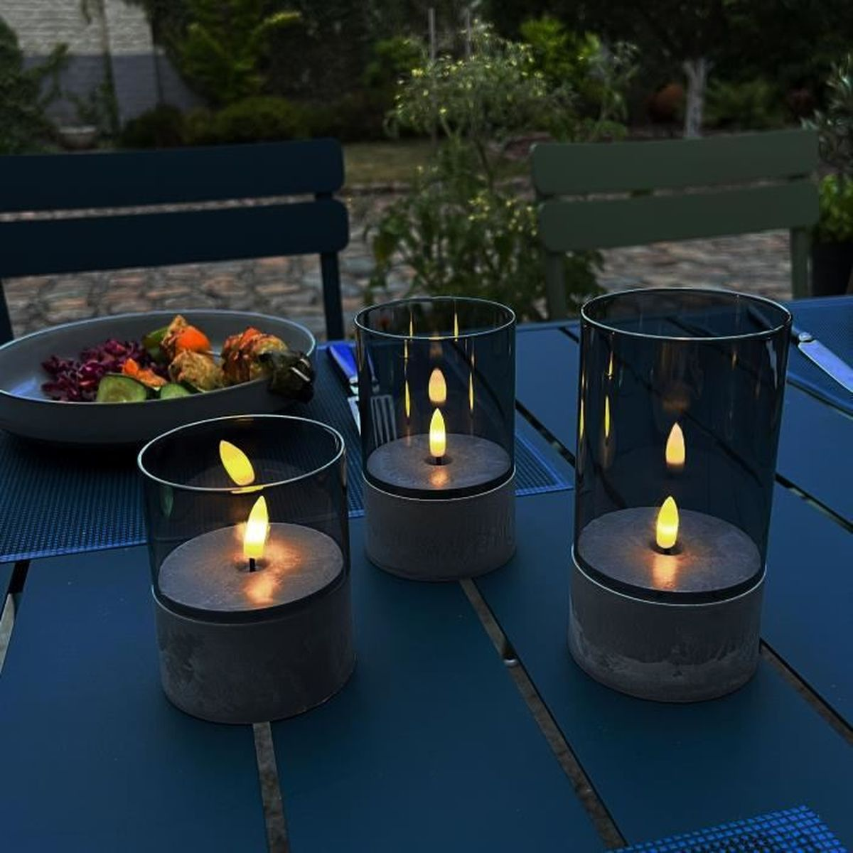 Drei Laternen mit Kerzenlicht auf einem Tisch mit Essen im Hintergrund.