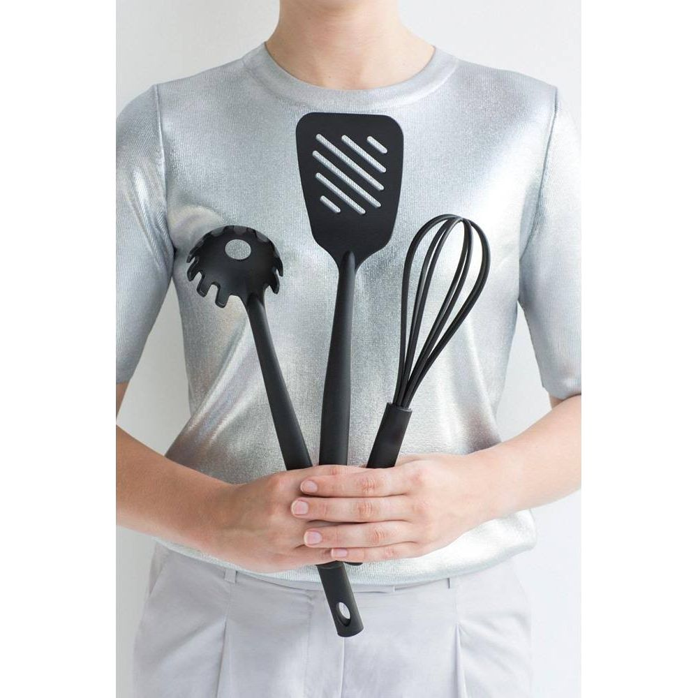 Una persona tiene tre utensili da cucina neri: mestolo per spaghetti, spatola e frusta.