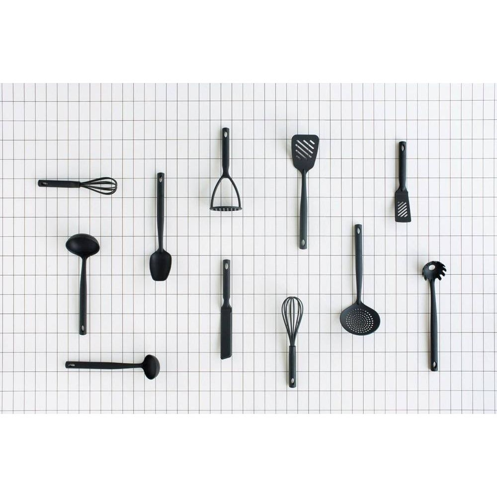 Utensili da cucina neri su sfondo a griglia bianca: frusta, mestolo, spatole, schiacciapatate.