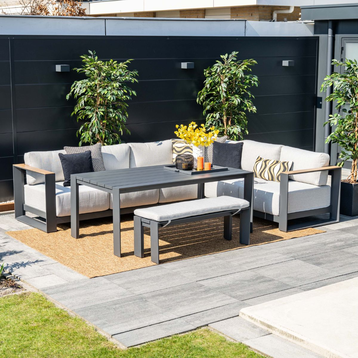 Moderne buitenruimte met beige loungebank, grijze tafel en kussens.