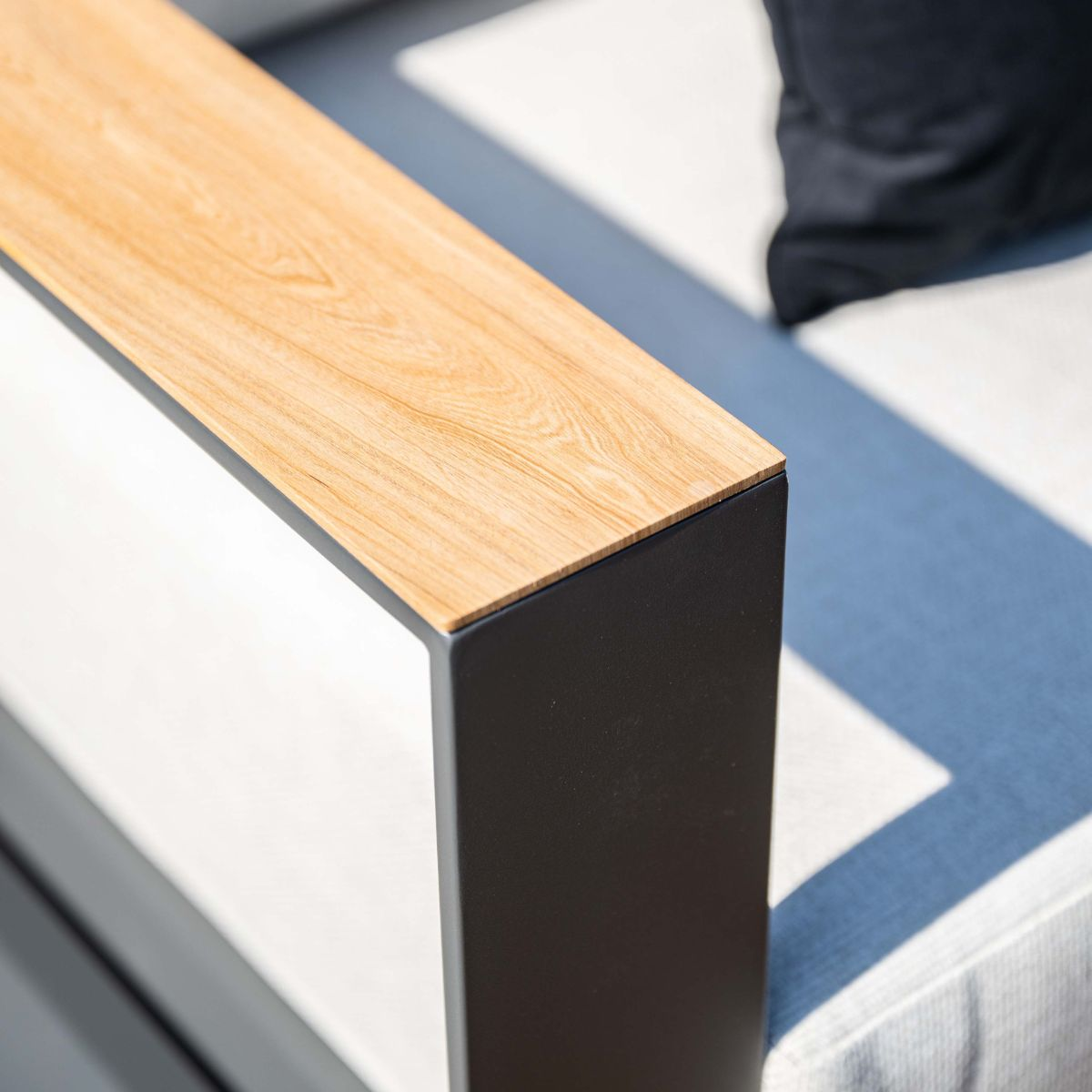 Een houten accent op een zwart frame van buitenmeubilair, met kussens op de achtergrond.