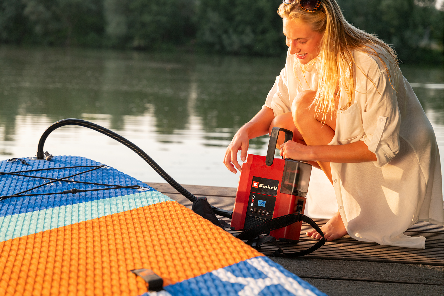 Frau mit aufblasbarem Paddelbrett und Pumpe am Wasser.