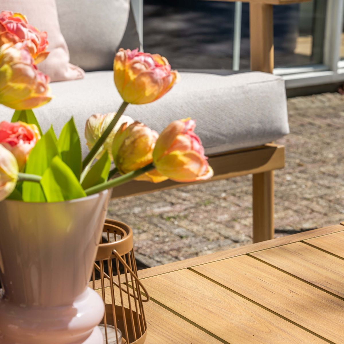 Een roze vaas met tulpen staat op een houten tafel naast een lantaarnstandaard.